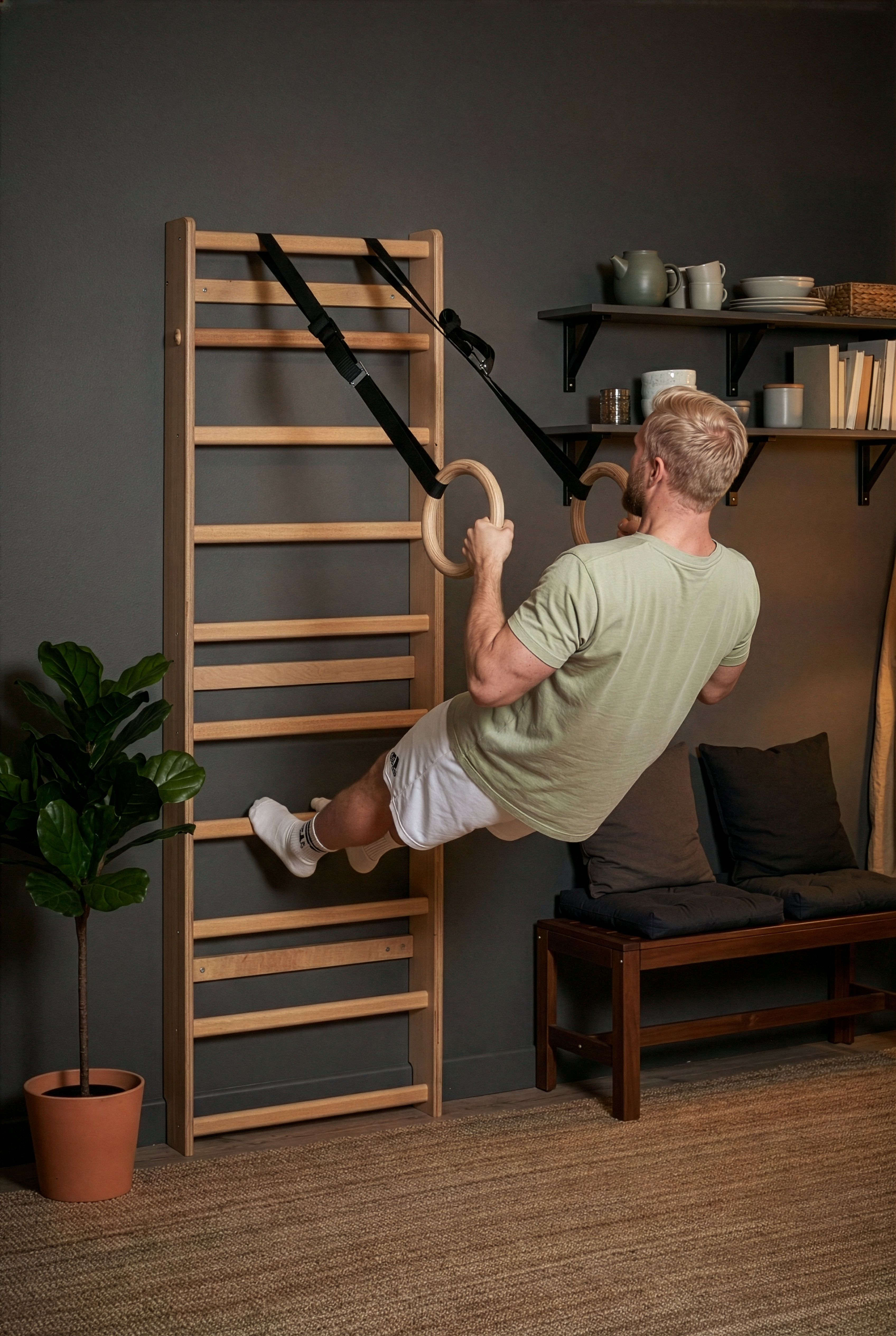 Man using wooden gymnastic rings in a home setting with a ladder and shelves in the background.