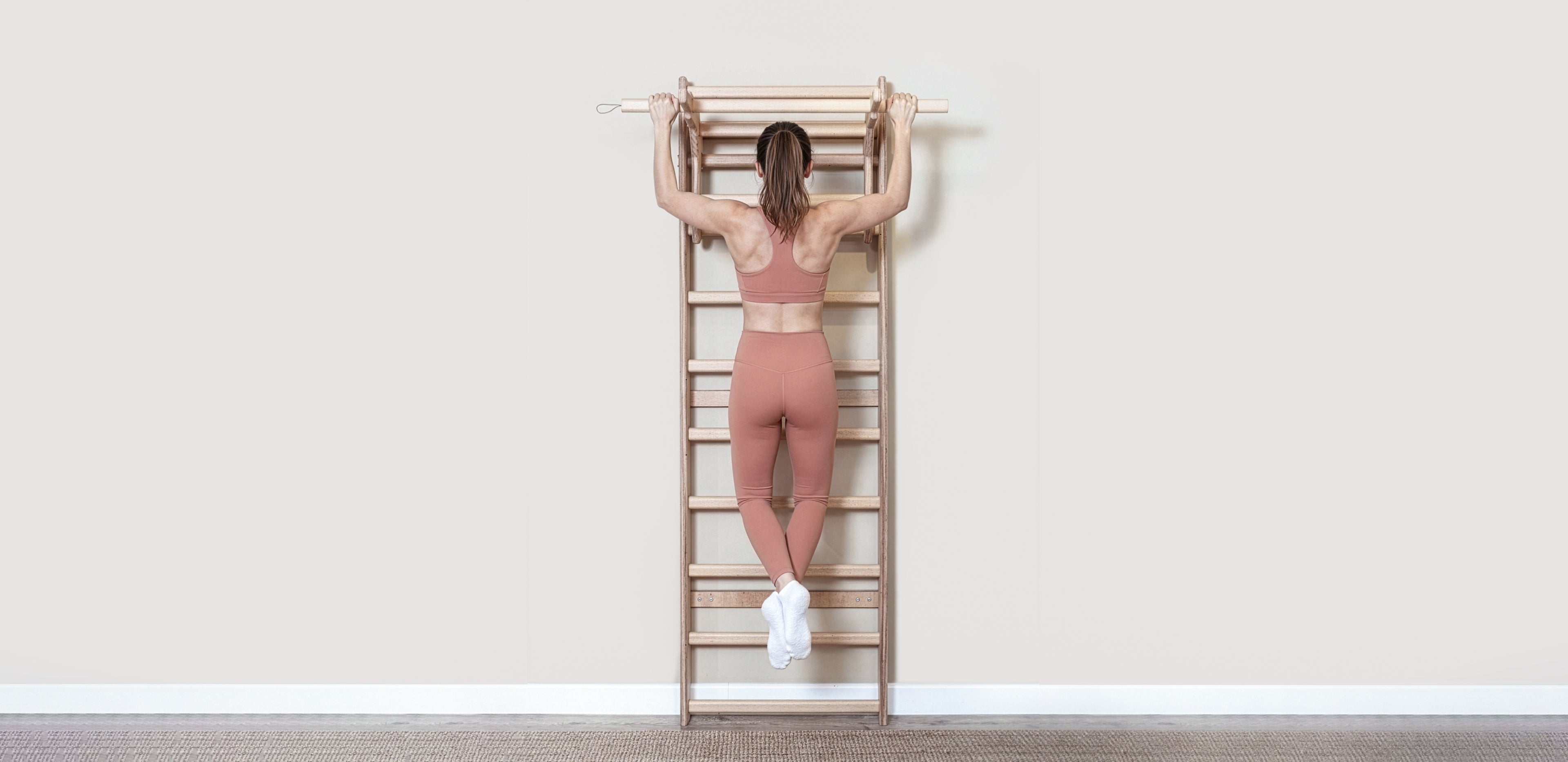 Fit model performing calisthenics exercises on a MowoFit modular wall bar, showcasing the premium handcrafted solid Beech wood design in a modern minimalist space.